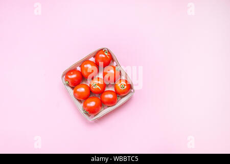 Red Cherry Tomaten in einem geflochtenen Korb auf einem rosa Hintergrund Stockfoto