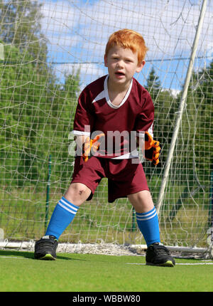 Torwart Kind wartet eine Kugel von einem Elfmeter auf ein Fußballstadion zu fangen. Fröhliche kleine Junge mit Ingwer Haar. Fußballspieler Sport Kleidung Stockfoto