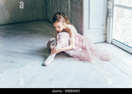 Junge Ballett Tänzerin Mädchen im Tanz Klasse. Schöne anmutige Ballerina in rosa Tutu Rock setzt auf pointe Schuhe in der Nähe von großes Fenster in Weiß lig Stockfoto