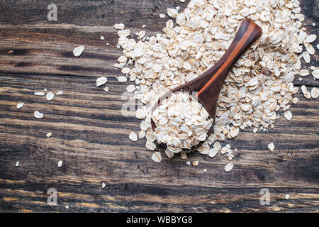 Gesunde Roh ungekocht schnelle Haferflocken in einem Löffel aus Holz Über Holz Tisch Hintergrund. Von der Ansicht von oben geschossen. Stockfoto