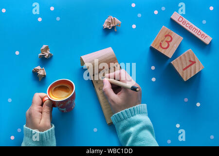 Weihnachten Hände Liste und der Frau mit Stift, Notizbuch, Kalender und Kaffee auf Blau pastell Tabelle Ansicht von oben. Flach Stil, blaues Papier Hintergrund mit Stockfoto