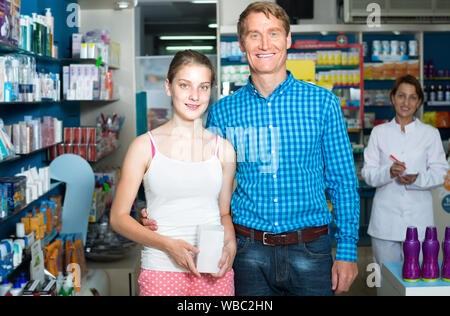 Lächelnd Vater mit Teenager Tochter Hilfe von Berater in pharmazeutischen Store Stockfoto