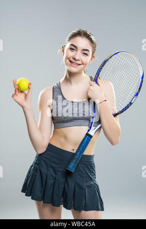 Zugeschnittenes Bild von einer selbstbewussten Frau tennis Spieler mit Schläger und Ball über grauer Hintergrund Stockfoto