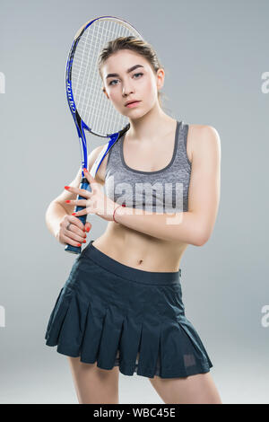 Zugeschnittenes Bild von einer selbstbewussten Frau tennis Spieler mit Schläger und Ball über grauer Hintergrund Stockfoto