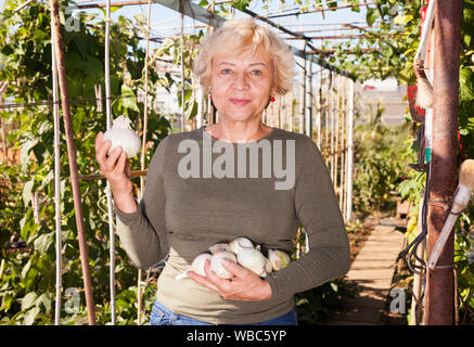 Portrait von positiven Senior woman holding weiße Zwiebel in der Hand im Garten Stockfoto