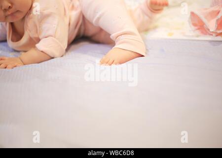 Baby kriechen und um Rollen auf dem Bett. Weich und Zärtlichkeit kleines Baby Füße Festlegung auf die weiche Bettwäsche. das Aufwachsen in einer liebevollen Familie Komfort. Stockfoto