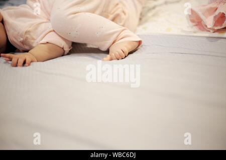 Baby kriechen und um Rollen auf dem Bett. Weich und Zärtlichkeit kleines Baby Füße Festlegung auf die weiche Bettwäsche. das Aufwachsen in einer liebevollen Familie Komfort. Stockfoto