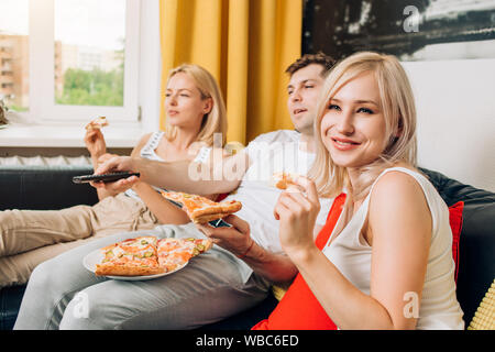 Zwei blonde kaukasischen schöne Frau und Mann zu Hause relaxen, Fernsehen, sitzen auf dem Sofa und genießen leckere Pizza. Selektive konzentrieren. Fast food, enjo Stockfoto