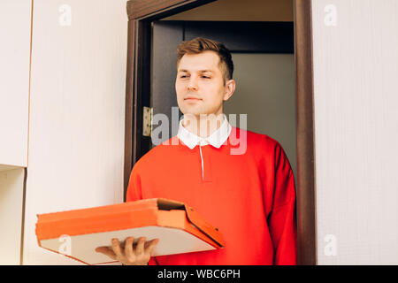 Foto von Happy stattlichen kaukasischen Mann aus Lieferservice in rote Uniform, Essen bestellen, pizza box. Lieferung, Fast food Konzept. Pizza de Stockfoto