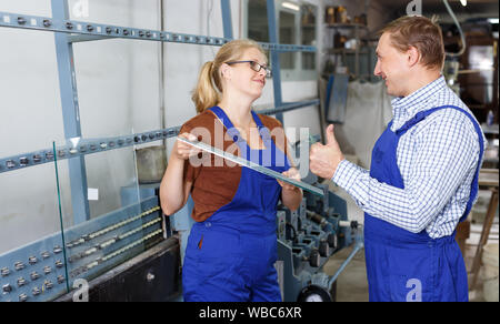 Aktive Frau und ihr männlicher Kollege arbeitet in der gläsernen Werkstatt Stockfoto