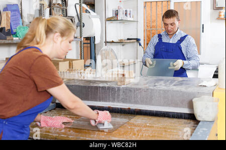 Froh, dass männliche Arbeitnehmer mit weiblichen Lehrling arbeiten auf Glas Waschmaschine in der Werkstatt Stockfoto