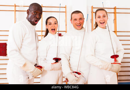 Gruppe positiver Fechter stehen mit Folien zusammen an fechten Training Stockfoto