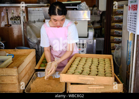 Ein junges Mädchen macht grüne Reiskuchen, Mochi, mit Beifuß, gefüllt mit anko, einer süßen roten Paste aus Azuki-Bohnen und bestäubt mit Kinako-Mehl Stockfoto