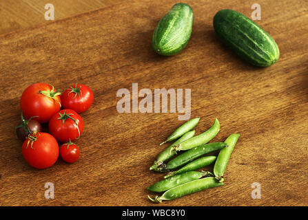 Blick von oben auf die frische organische home Gemüse auf einem braunen Holztisch. Tomaten, Gurken und Erbsen mit Kopie Raum Stockfoto