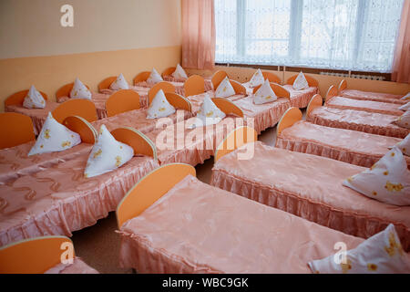 Zustell- und Kinderbetten sind in einem hellen Schlafsaal von einem Baumschule. eine Menge von Kinderbetten. Stockfoto