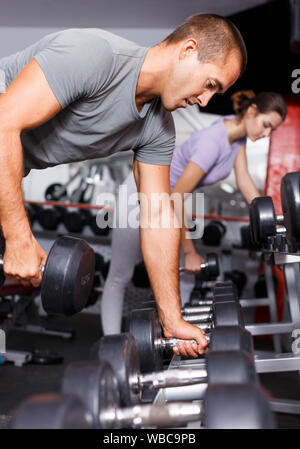 Sportlicher Mann mit Kurzhanteln auf Regal für weightlifting Equipment gym Stockfoto