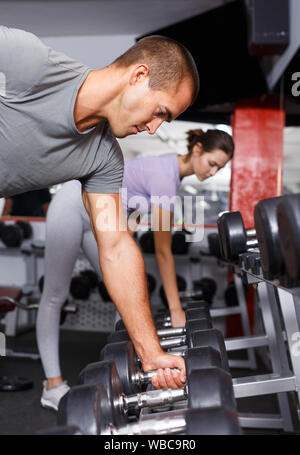 Sportlicher Mann mit Kurzhanteln auf Regal für weightlifting Equipment gym Stockfoto