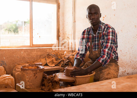 Afrikanische jungen Mann auf Arbeit an Töpferei Rad in Workshop konzentriert, schafft neue Objekt Stockfoto