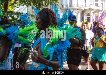 Maskierten hinter einem Lkw. Die wichtigsten Ereignisse der Notting Hill Carnival 2019 erhielt unterwegs am Sonntag, mit über einer Million revellers schlagen die Straßen von West London, unter den Schwimmern, maskierten, Steel Bands und Sound Systeme. Stockfoto