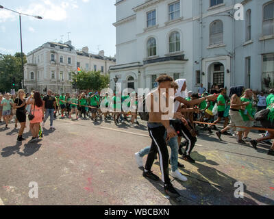 Maskierten sich entlang einer Straße hinter einem Sound System Truck. Die wichtigsten Ereignisse der Notting Hill Carnival 2019 erhielt unterwegs am Sonntag, mit über einer Million revellers schlagen die Straßen von West London, unter den Schwimmern, maskierten, Steel Bands und Sound Systeme. Stockfoto