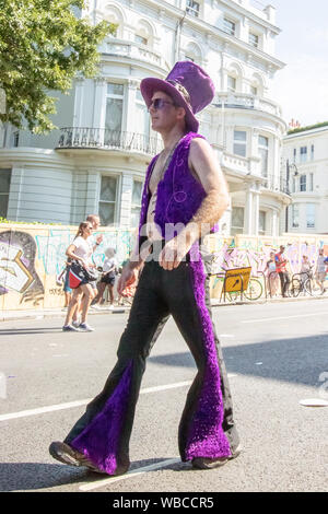 Ein Mann Spaziergänge entlang einer Straße in sein Kostüm. Die wichtigsten Ereignisse der Notting Hill Carnival 2019 erhielt unterwegs am Sonntag, mit über einer Million revellers schlagen die Straßen von West London, unter den Schwimmern, maskierten, Steel Bands und Sound Systeme. Stockfoto