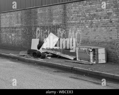 Urban Schuttplatz, Abfall illegal entsorgt auf einem Gehsteig neben einer Wand mit Graffiti in der Stadt und Umgebung. Stockfoto