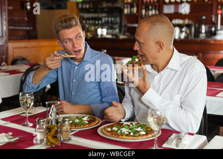 Zwei männliche Freunde genießen leckere Pizza im gemütlichen Restaurant Stockfoto
