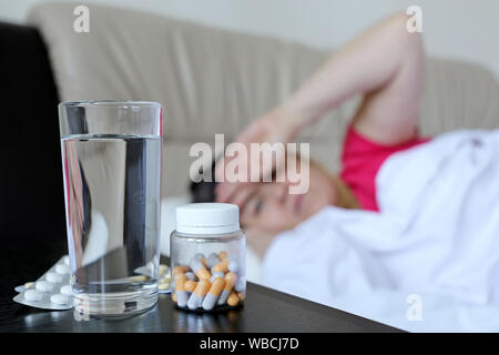 Kranken Frau liegt in einem Bett Hand auf ihre Stirn, Kälte und Grippe Saison. Pillen und Wasser Glas im Vordergrund, Konzept der Krankheit, Fieber Stockfoto