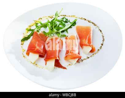 Spanisch leckeres Gericht Rollen des Prosciutto di Parma mit Melone mit Rucola an Platte serviert, ganz nah. Auf weissem Hintergrund Stockfoto