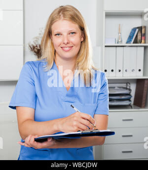 Lächelnd weibliche Krankenschwester in formale Abnutzung Registrierung Informationen in Form Stockfoto