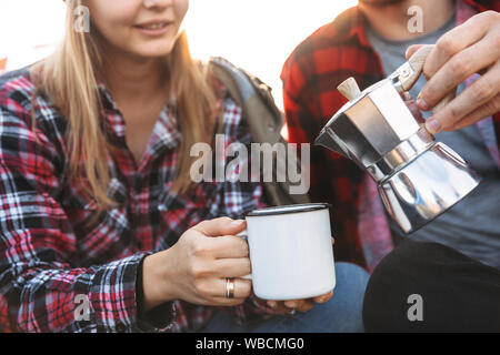 Zugeschnittenes Bild eines attraktiven jungen Paar ruht, während im Zelt, im Freien sitzen, Kaffee in eine Tasse gießen Stockfoto