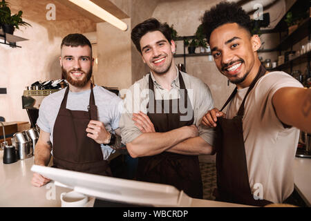 Drei fröhliche Männer baristas steht hinter der Theke im Coffee Shop, ein selfie Stockfoto