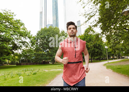 Foto von stattlicher Mann mit Sportswear Musik hören mit Kopfhörern beim Laufen im City Park Stockfoto