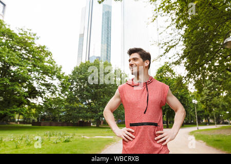 Fotos von glücklichen Mann, sportswear Musik hören mit Kopfhörern, während Sie im City Park arbeiten Stockfoto