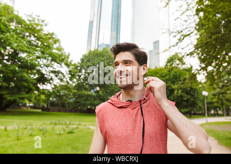 Fotos von lächelnden Mann, sportswear Musik hören mit Kopfhörern, während Sie im City Park arbeiten Stockfoto