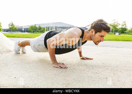 Bild von stattlicher Mann in Sportkleidung und tun Push-ups am grünen Park im Freien in Morgen Stockfoto