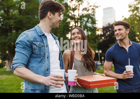 Gruppe von fröhlichen jungen Freunde zu Fuß in der City Park, Pizza und Getränke Stockfoto