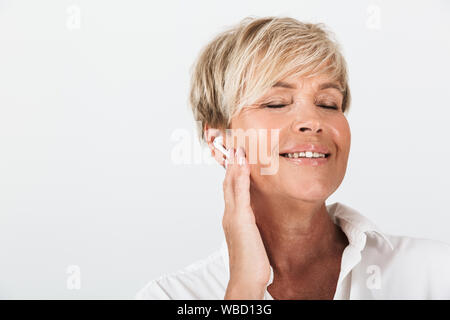 Portrait Nahaufnahme der glücklichen erwachsenen Frau mit kurzen blonden Haaren tragen earpods auf weißem Hintergrund im Studio isoliert Stockfoto