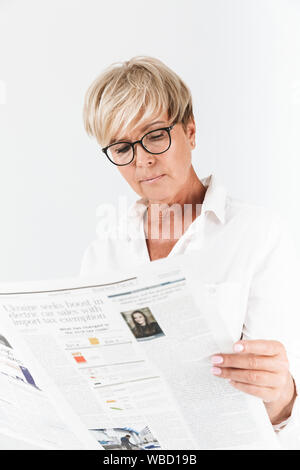 Portrait von Konzentriertem erwachsenen Frau tragen Brillen lesen Zeitung isoliert auf weißem Hintergrund im Studio Stockfoto