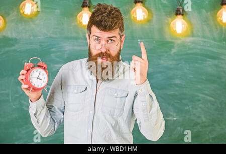 Lehrer in Brillen hält Wecker. Disziplin Konzept. Mann mit Bart und Schnurrbart auf strengen Gesicht stand im Klassenzimmer. Bärtige hipster hält, Warnung mit Zeigefinger, kopieren. Stockfoto