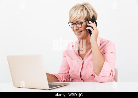 Portrait der kaukasischen Frau mittleren Alters tragen Brillen mit Handy und Laptop auf weißem Hintergrund Stockfoto