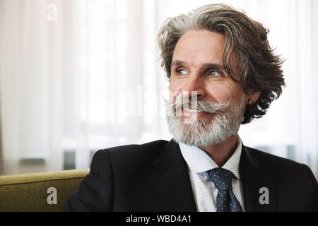 Bild eines schönen fröhlichen Happy älterer grauhaariger business Mann im Sessel zuhause zu Hause sitzen. Stockfoto