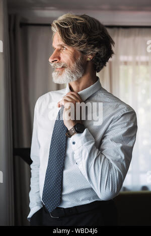 Bild von einem stattlichen älterer grauhaariger Geschäftsmann im Innenbereich in formelle Kleidung an Fenster gekleidet. Stockfoto