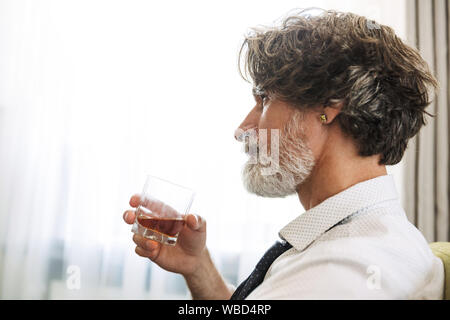 Seitenansicht Foto von einem schweren älterer grauhaariger business Mann im Sessel zuhause zu Hause Alkohol sitzen. Stockfoto