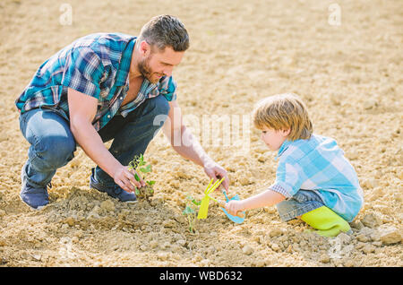 Kleiner Junge Kind helfen Vater in der Landwirtschaft. reichen natürlichen Boden. Eco Farm. Vater und Sohn Blumen Pflanzen im Boden. neues Leben. Böden, Düngemitteln. happy Earth Day. Stammbaum. Tag der Erde. Das Sitzen auf dem Boden. Stockfoto