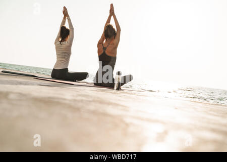 Foto von der Rückseite der konzentrierten sich junge Frauen in Trainingsanzügen meditieren und die Handflächen zusammen beim Üben von Yoga am Morgen im Freien Stockfoto