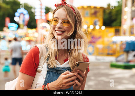 Bild eines lächelnden Jungen fröhliche blonde Frau im Vergnügungspark mit Handy. Stockfoto