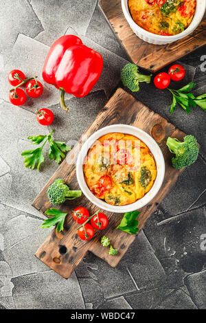 Frittata mit Brokkoli in Keramik. Frittata mit Brokkoli, süßer Paprika und Tomaten in zwei keramischen Formen zum Backen. Italienische Omelette mit v Stockfoto