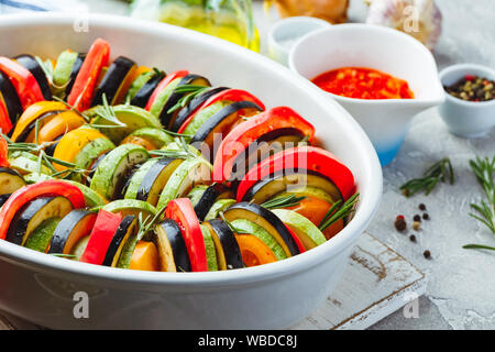 Vegetarische Rohkost Ratatouille aus Auberginen, Zucchini, Tomaten und Paprika Sauce und Tomaten mit Kräutern in keramischen Form vor dem Backen. Rustikale s Stockfoto