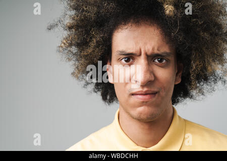 Foto Nahaufnahme von Verspannten kaukasischen Mann mit Afro Frisur stirnrunzelnd an Kamera mit traurigen Blick über grauer Hintergrund Stockfoto